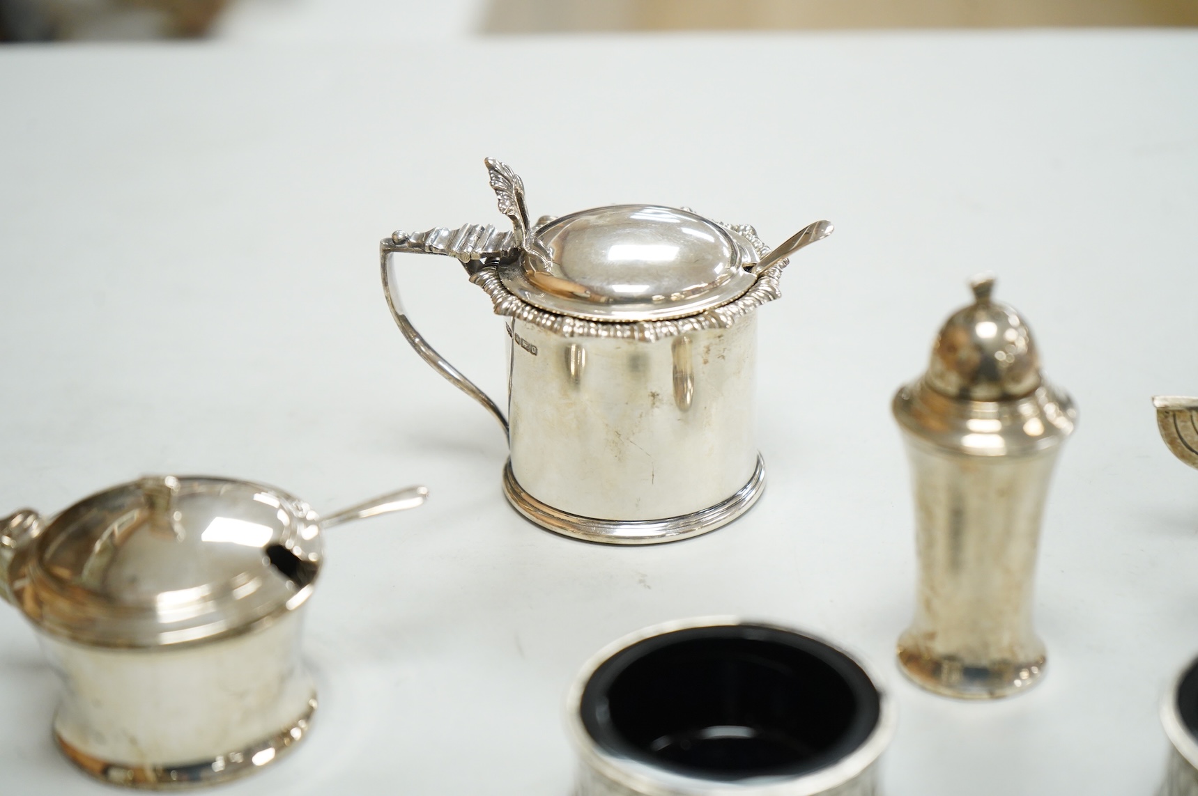 A George V Art Deco three piece silver condiment set and two spoons by William Adams Ltd, Birmingham, 1935, together with a pair of late Victorian pierced silver salts with blue glass liners and an Edwardian silver musta